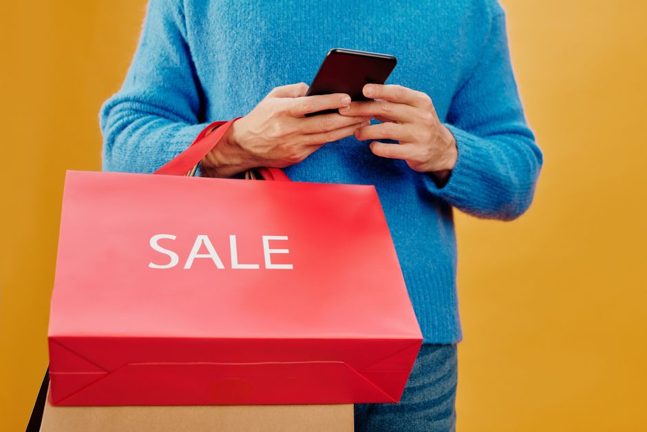 Close-up of a man holding a sale bag and smartphone, symbolizing shopping and discounts.