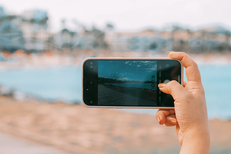 Hand holding smartphone capturing a scenic beach view in Palma de Mallorca.