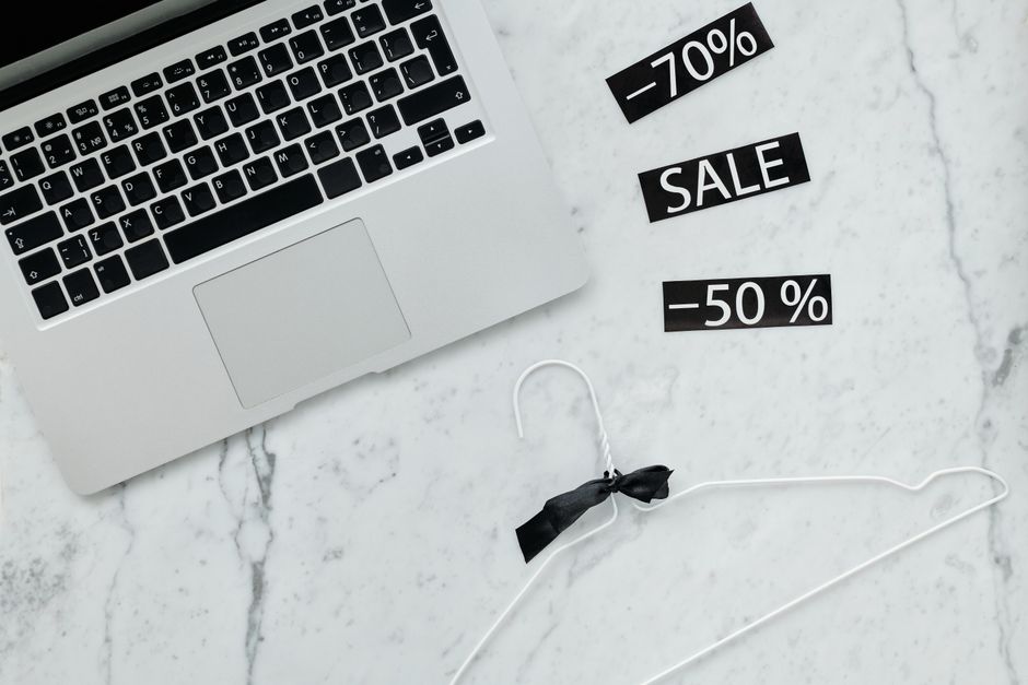 Flat lay of a laptop, hanger, and sale stickers on a marble desk, ideal for Black Friday themes.