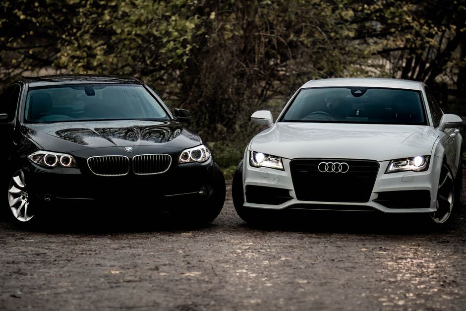 Black BMW and white Audi luxury sedans parked outdoors on a gravel path.