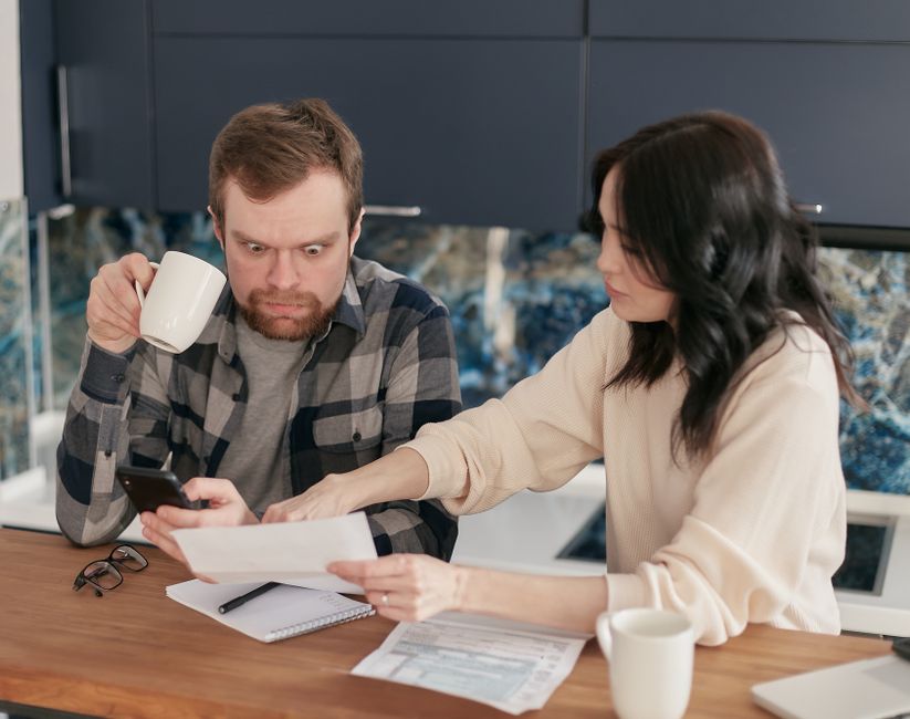 A couple reviews household bills in a kitchen, appearing concerned and focused.