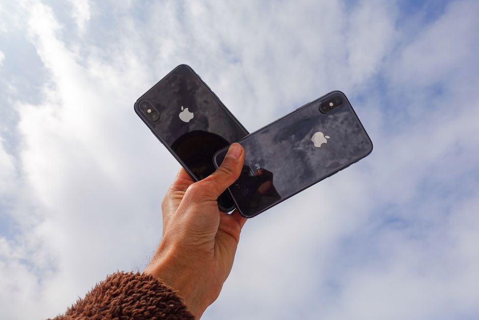 Close-up of a hand holding two smartphones against a cloudy sky, showcasing modern technology.