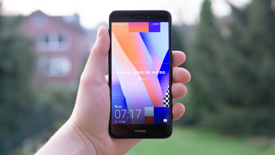 Hand holding a Huawei smartphone displaying a colorful screen outdoors in Germany.